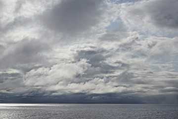 The sun pierces through gathering storm clouds over the Gulf of Alaska.