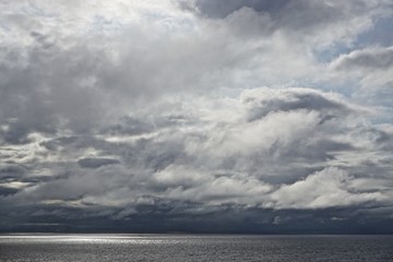 The sun pierces through gathering storm clouds over the Gulf of Alaska.