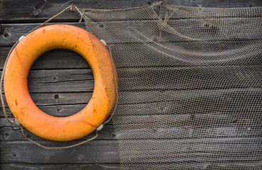 A bright orange life preserver and fishing net hang on a very old, cracked gray wooden wall.