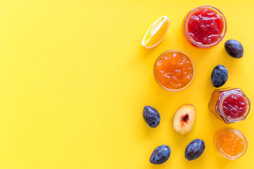 Jams different tastes made of fruits and berries near pieces of fruits on yellow background top view copy space