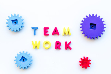 Teamwork concept. Text teamwork lined with colored letters near toy gears on white background top view copyspace