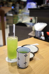 Japanese hot and cold green tea glass on a wooden table with 2 empty plates and the background is a blurred shop.