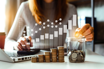 businesswoman holding coins putting in glass with using smartphone and calculator to calculate ...