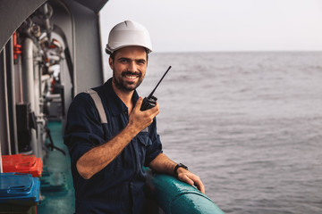 Marine Deck Officer or Chief mate on deck of vessel or ship . He holds VHF walkie-talkie radio in hands. Ship communication