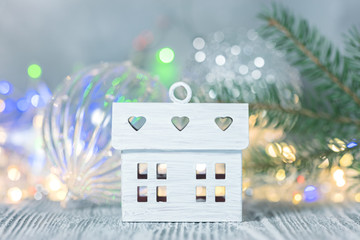 small decorative house against blurred glowing holiday lights background and fir tree branch