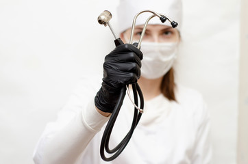a woman in a white robe, mask and black gloves, holding a stethoscope to listen to the patient's...