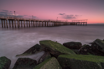 Obraz premium View on the pier from the sand beach with moss rocks at sunset,long exposure