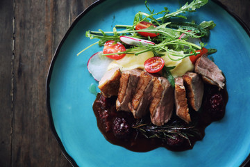 Duck confit with salad , baked apple and raspberry sauce served on wooden table