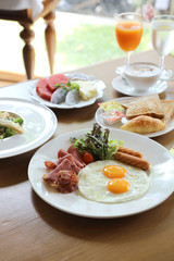 Breakfast set with fried eggs, bacon, sausages, beans, toasts, fresh salad and fruit on wood table