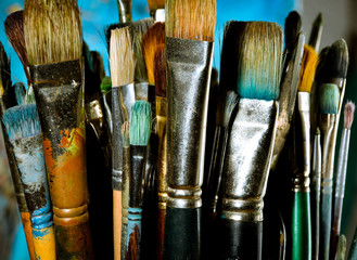 Dirty artist oil paint brushes in stacks against blue background - landscape orientation 
