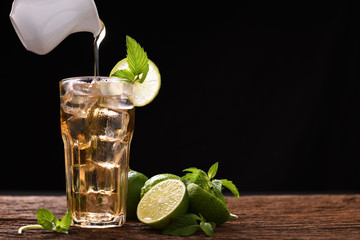 Iced lime honey tea in glass with mint and slice lime on wooden table and black background
