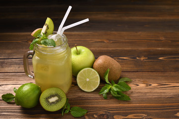 Mixed lime,kiwi,apple juice with slice fruits in jug on wooden table on black background