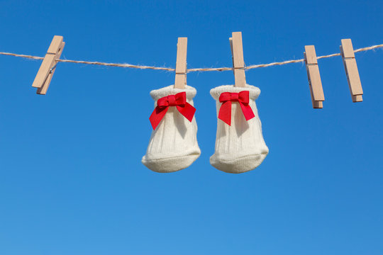 青空に木製洗濯挟みで吊るされた赤いリボンの新生児用靴下。赤ちゃん、育児、出産、幸せ、愛イメージ