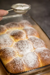 Hand with sieve of sugar and bunch of buns