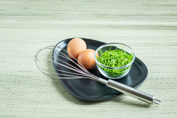 Acacia Pennata (Climbing Wattle) in small glass bowl with two eggs and a whisk on black plate
