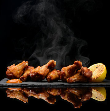 Hot and spicy bbq chicken wings with dip and hot sauce on black stone plate 