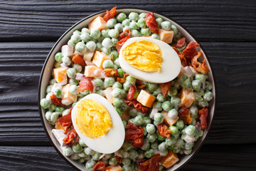 English salad of fresh green peas with eggs, bacon and cheese dressed with cream sauce close-up in a bowl. horizontal top view