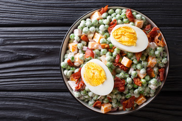English green pea salad with boiled eggs, onions, bacon and cheddar cheese with cream sauce closeup in a bowl. horizontal top view