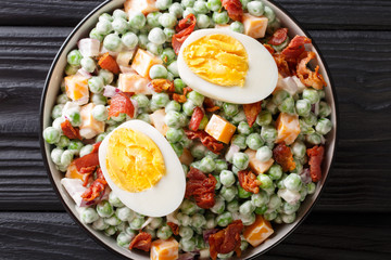 Easy English salad of raw green peas with boiled eggs, bacon and cheddar cheese with sauce close-up...