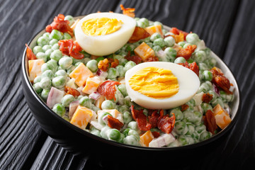 English green pea salad with boiled eggs, onions, bacon and cheddar cheese with cream sauce closeup in a bowl. horizontal