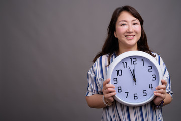 Portrait of mature beautiful Asian businesswoman holding clock