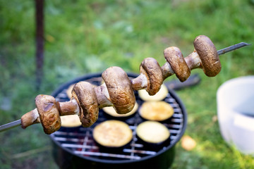 A skewer of grilled mushrooms on the background of the grill with eggplant