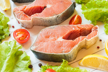 Raw red fish steak with lemon and spices and fresh vegetables on light background.
