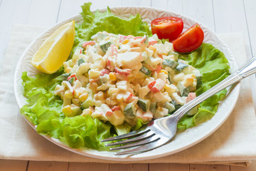 Salad with crab sticks, sweet corn, cucumber, eggs and mayonnaise on light table