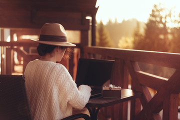 Young woman traveler sits at the terrace with a laptop against beautiful mountain scenery during journey.