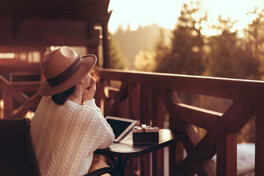 Young woman traveler sits at the terrace with a tablet against beautiful mountain scenery during journey.