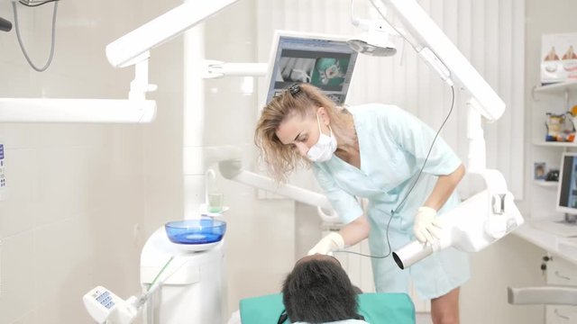 Woman dentist using x ray machine, patient lying on chair in dentistry. Young African American male with bad teeth. Medicine, health, stomatology concept.