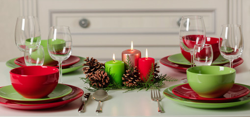 Merry Christmas and Happy New Year! Тable setting festive decor - green and red dishes, candles and fir cones. Knitted decor - Santa Claus knitted hats on the bottle with wine.