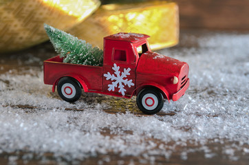 Obraz premium Red car, decorated with snowflake, carrying a Christmas fir tree on the snow background for celebrated Merry Christmas.