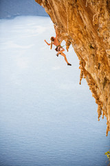 Young female rock climber in bikini hanging with one hand on cliff