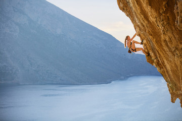 Young female rock climber on challenging route on cliff