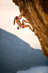 Young female rock climber wearing bikini on cliff at sunset