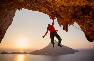  Mannelijke rotsklimmer die met één hand aan de klif hangt bij zonsondergang © Andrey Bandurenko