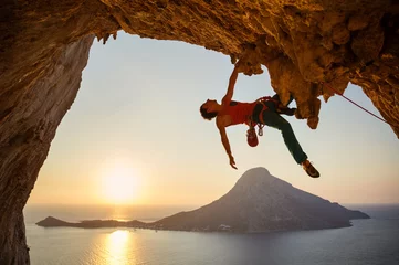 Gardinen Male rock climber hanging with one hand on challenging route at sunset © Andrey Bandurenko