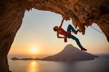Foto op Canvas Male rock climber hanging with one hand on challenging route on cliff at sunset © Andrey Bandurenko