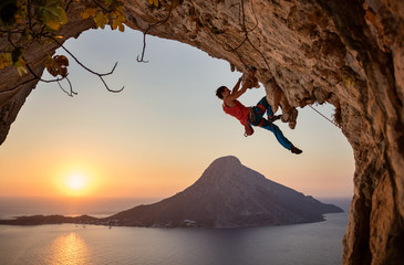 Male rock climber on challenging route on cliff at sunset