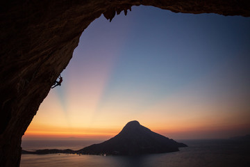 Male rock climber on overhanging cliff at sunset, with beautiful view of island in background