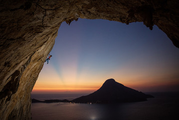 Male rock climber on overhanging cliff at sunset, with beautiful view of island in background