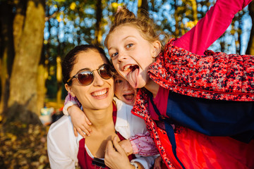 Cute two little daughter stick out fool around, playing on a piggy back ride with their mother....