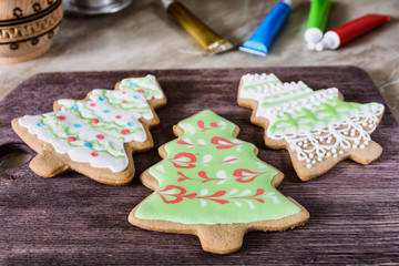 Three homemade Christmas gingerbread in the shape of a Christmas tree, just decorated with icing, are drying on a wooden board