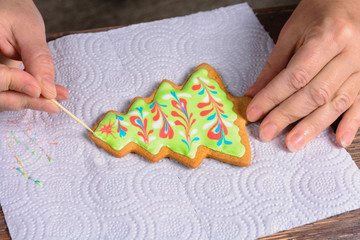 Making Christmas gingerbread at home. Female hand decorates Christmas tree-shaped gingerbread with colored icing 