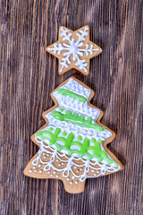 Colorful Christmas gingerbread in the shape of a Christmas tree and in the shape of a star decorated with white and green icing are  on a wooden board