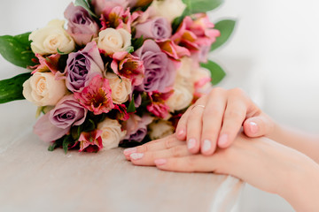 Female hands holding wedding flowers. Wedding ring and brides's dress.