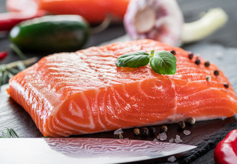 Fresh salmon fillets on black cutting board with herbs and spices.