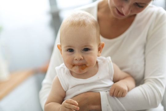 Mom feeds baby with spoon, cozy real interior