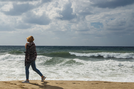 Woman tourist walking at coastline and looking to stormy sea
